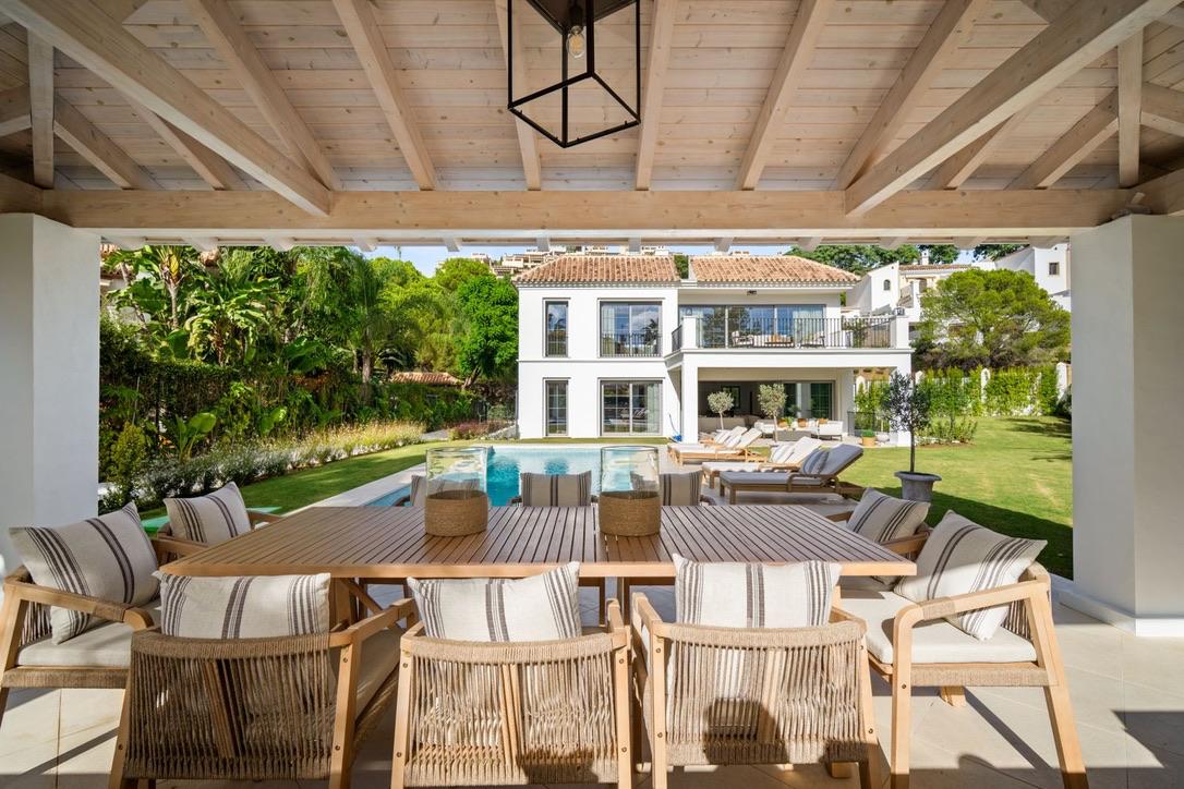 Covered terrace with a long dining table looking back at the villa